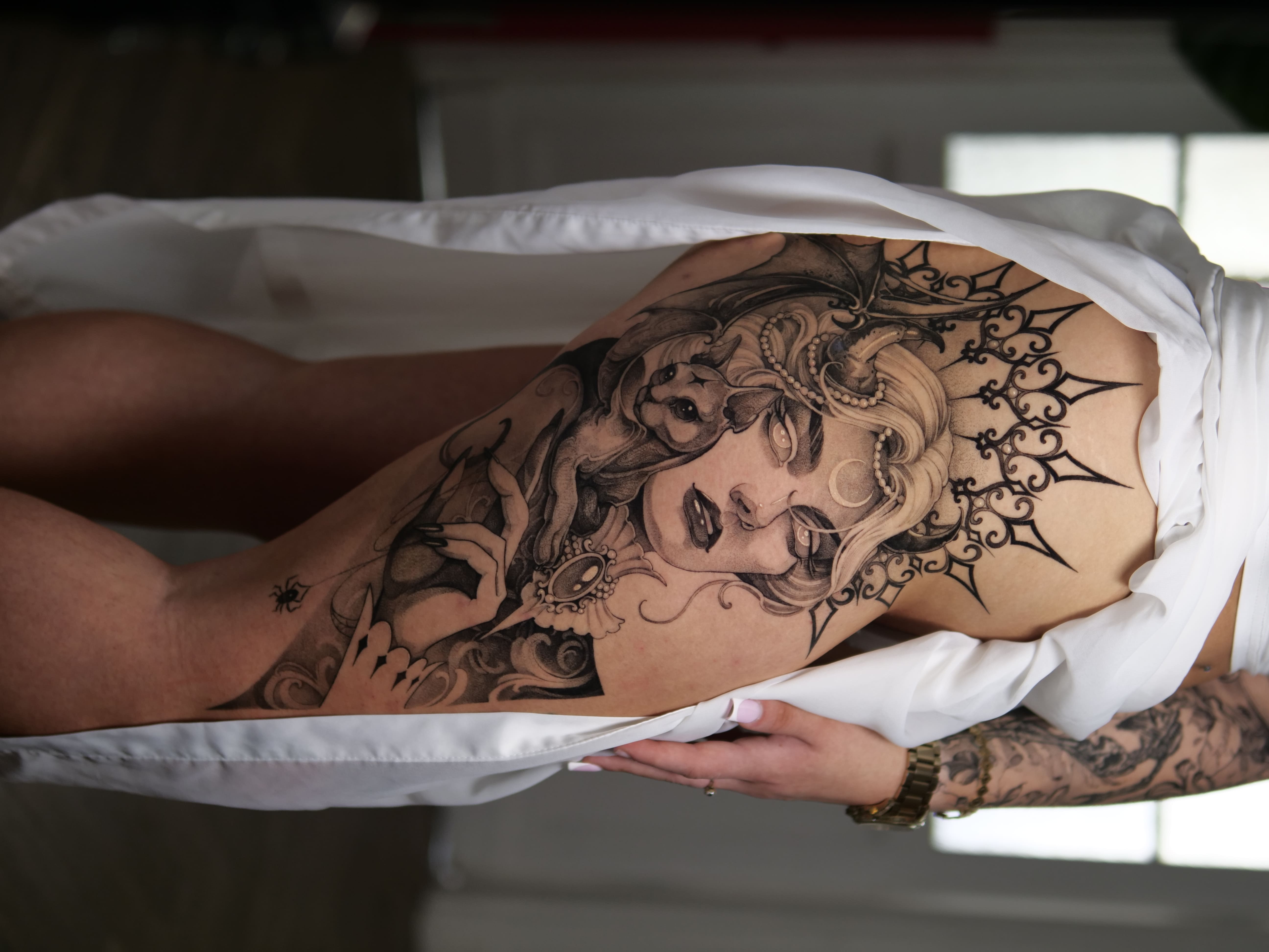 Na zdjęciu damski, kobiecy tatuaż na udzie, portret kobiety z elementami ornamentów, geometrii oraz biżuterii, wykonany w studio tatuażu Uroki w Warszawie